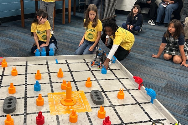 Three Oakland Christian students work with their robot on the competition mat.
