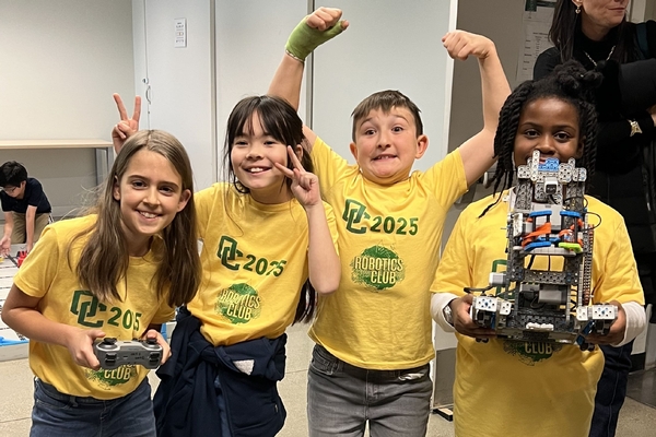 Four Oakland Christian students pose and smile triumphantly with their robot.