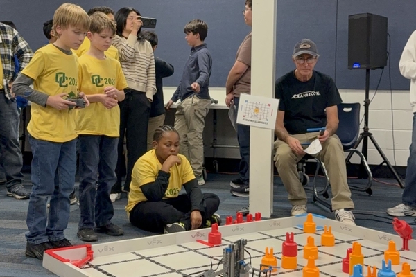 Three Oakland Christian boys work hard with their robot on the competition mat.