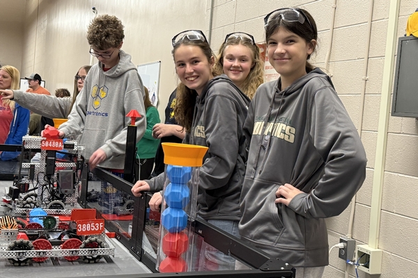 Oakland Christian students smile with their robot at a competition.