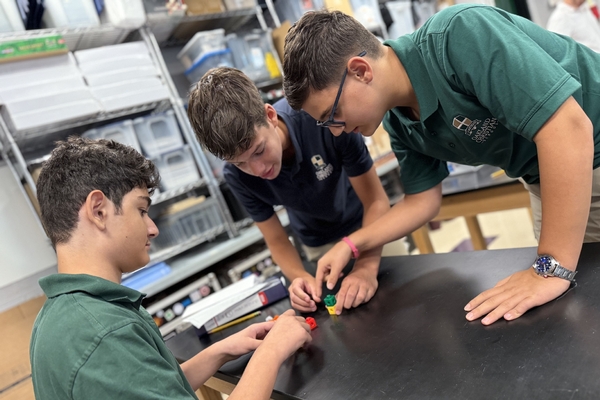 Three Oakland Christian students collaborate at their table with building cubes.