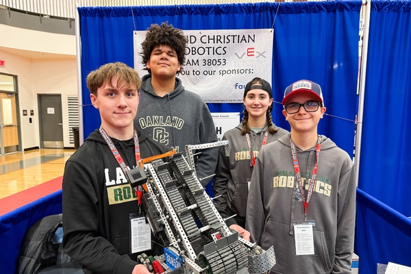 Four Oakland Christian students pose with their VEX robot at a competition.